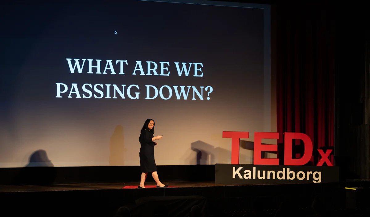 Dr. Roseann on the TEDx stage with the words What Are We Passing Down?