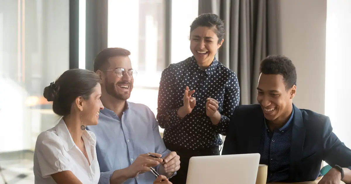 Four colleagues smiling together around laptop in modern office