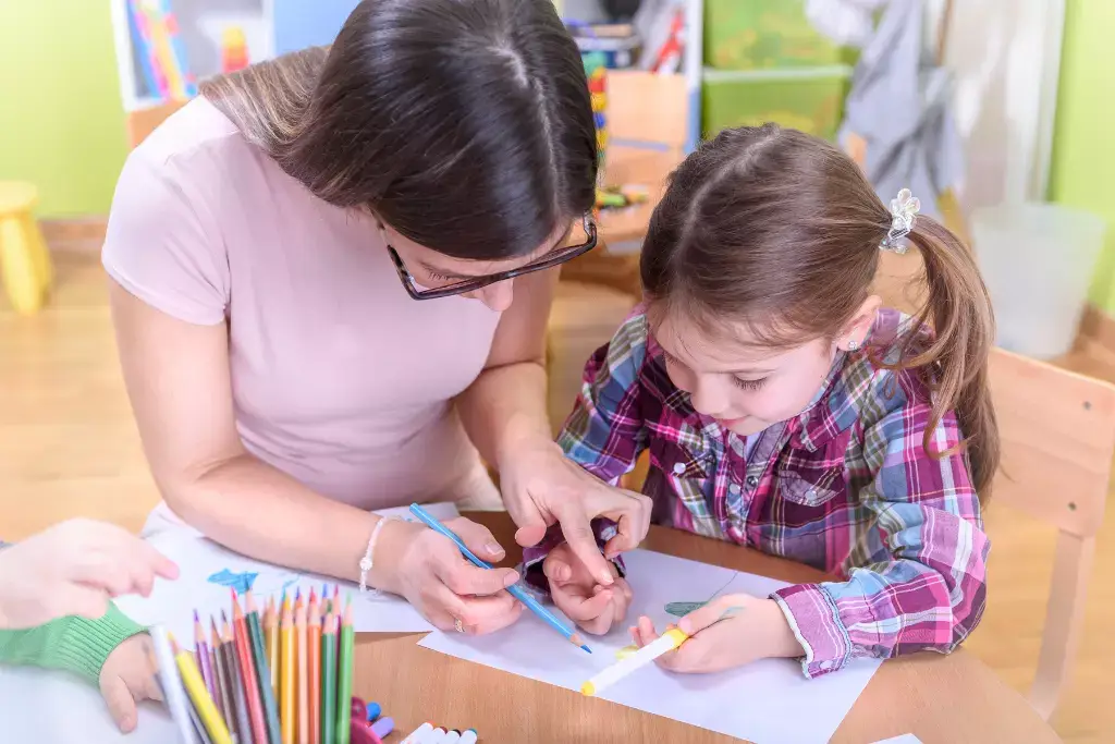 Adult and child doing a coloring activity together at a wooden table with colored pencils