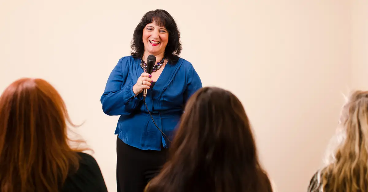 Woman in blue top speaking to audience with microphone at event