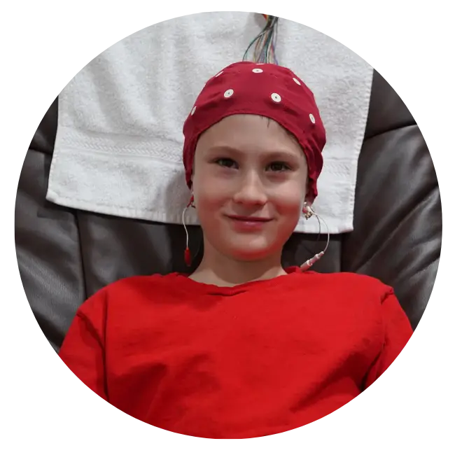 Child wearing red cap with neurofeedback electrodes, smiling