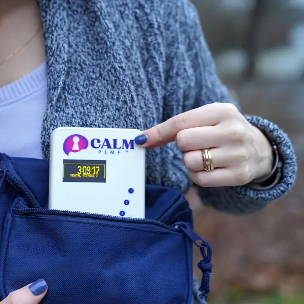 Close-up of hands holding white CALM PEMF device with charging port