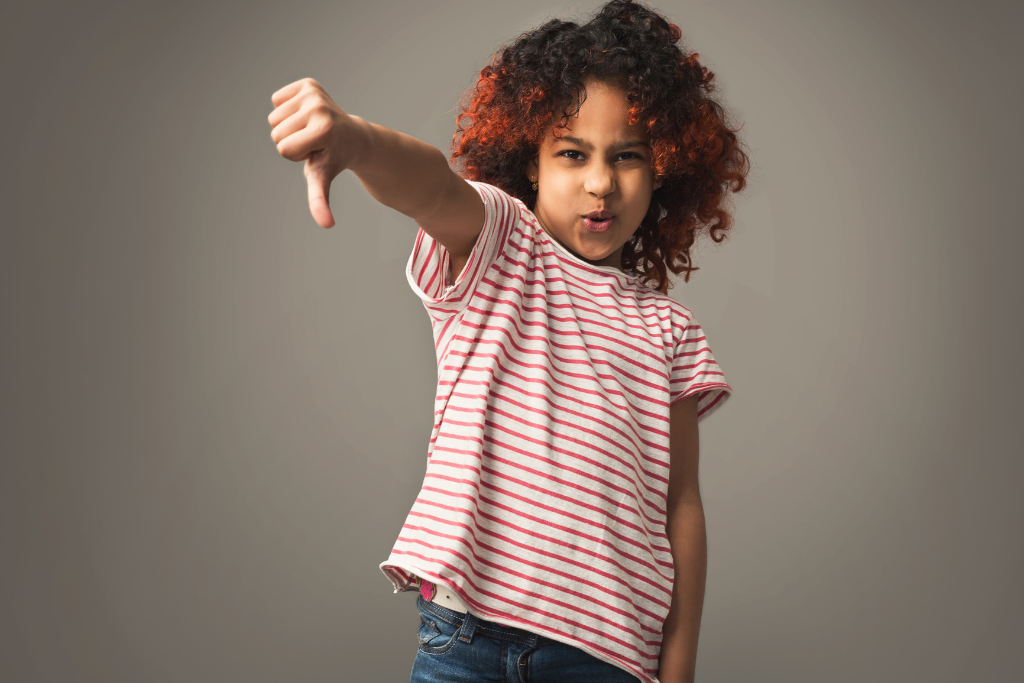 Child in striped shirt giving thumbs down gesture