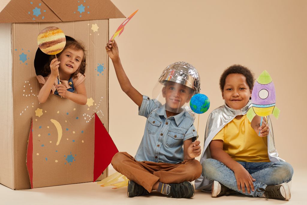 Children creating space-themed crafts with cardboard box and toys