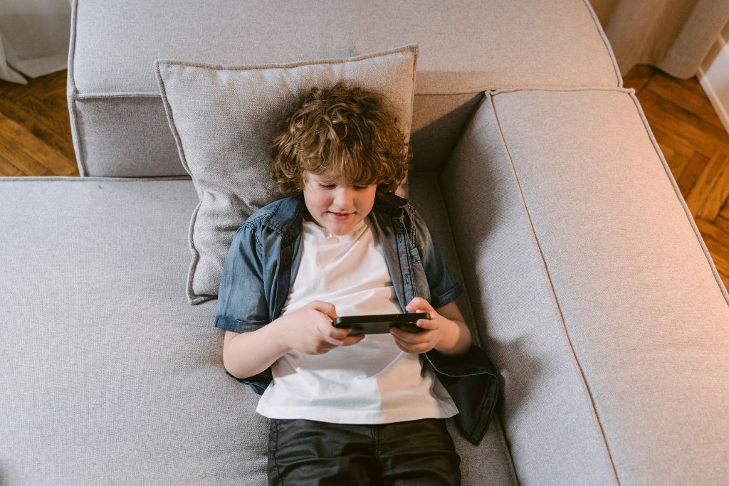 Child lying on couch using mobile device