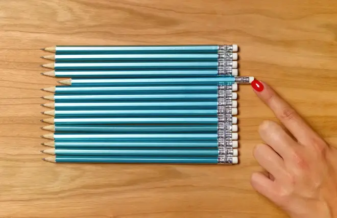 Hand holding row of teal pencils with erasers on wooden surface
