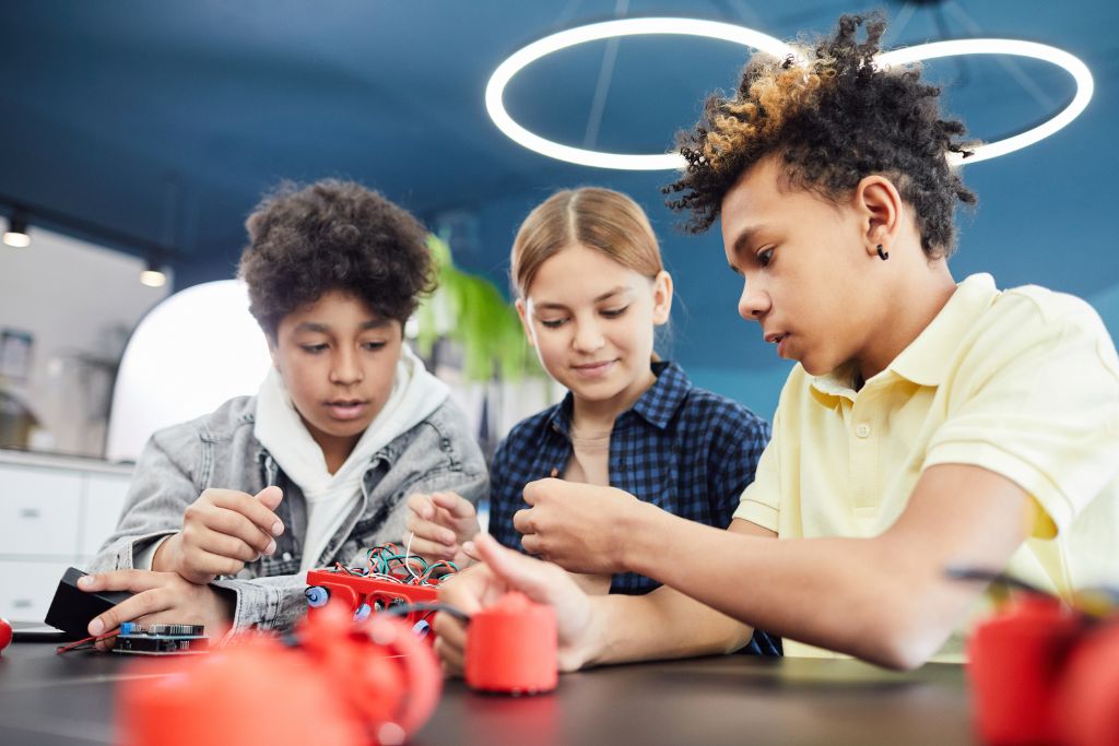 Three children around table with STEM robot building materials working together