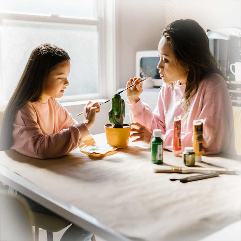 Mother and daughter painting together at table with natural light