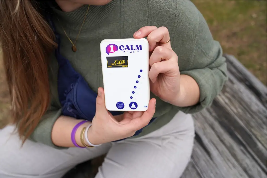 Hands holding white CALM PEMF device outdoors with child visible