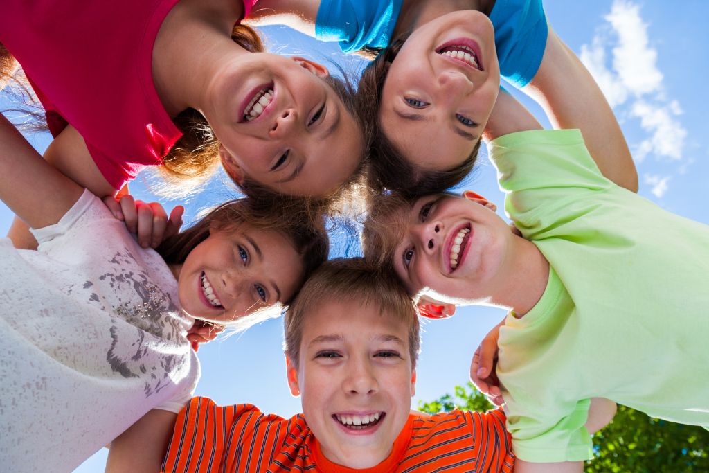 Group of happy children gathered together outdoors looking down at camera