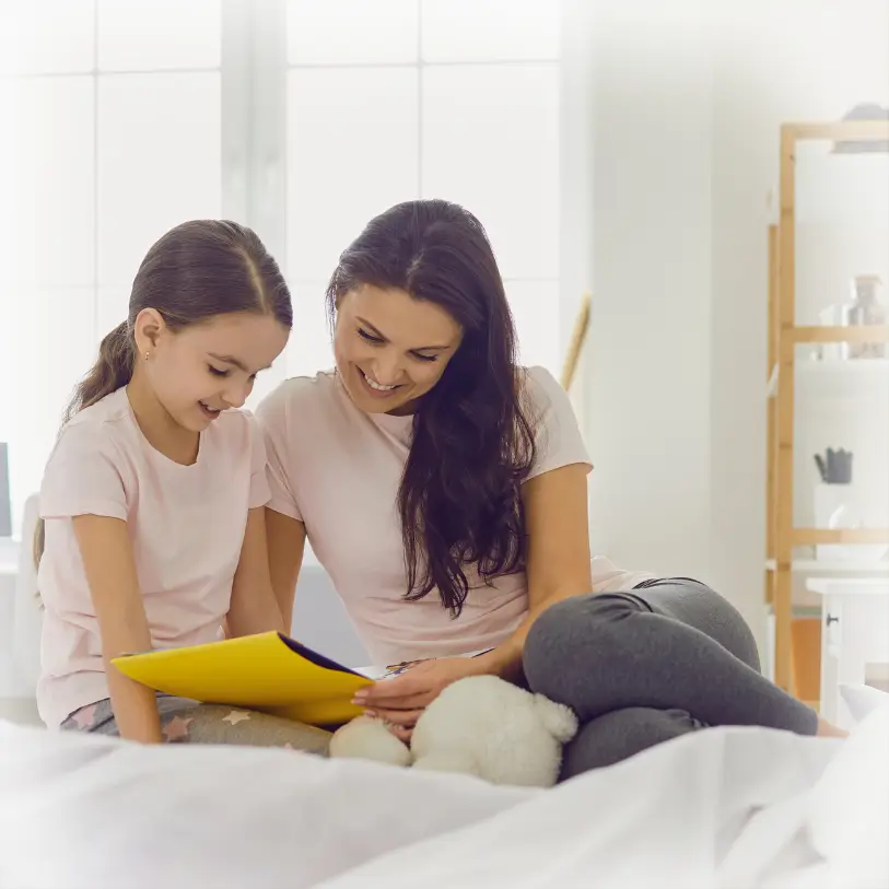 Mother and daughter reading yellow book together on bed