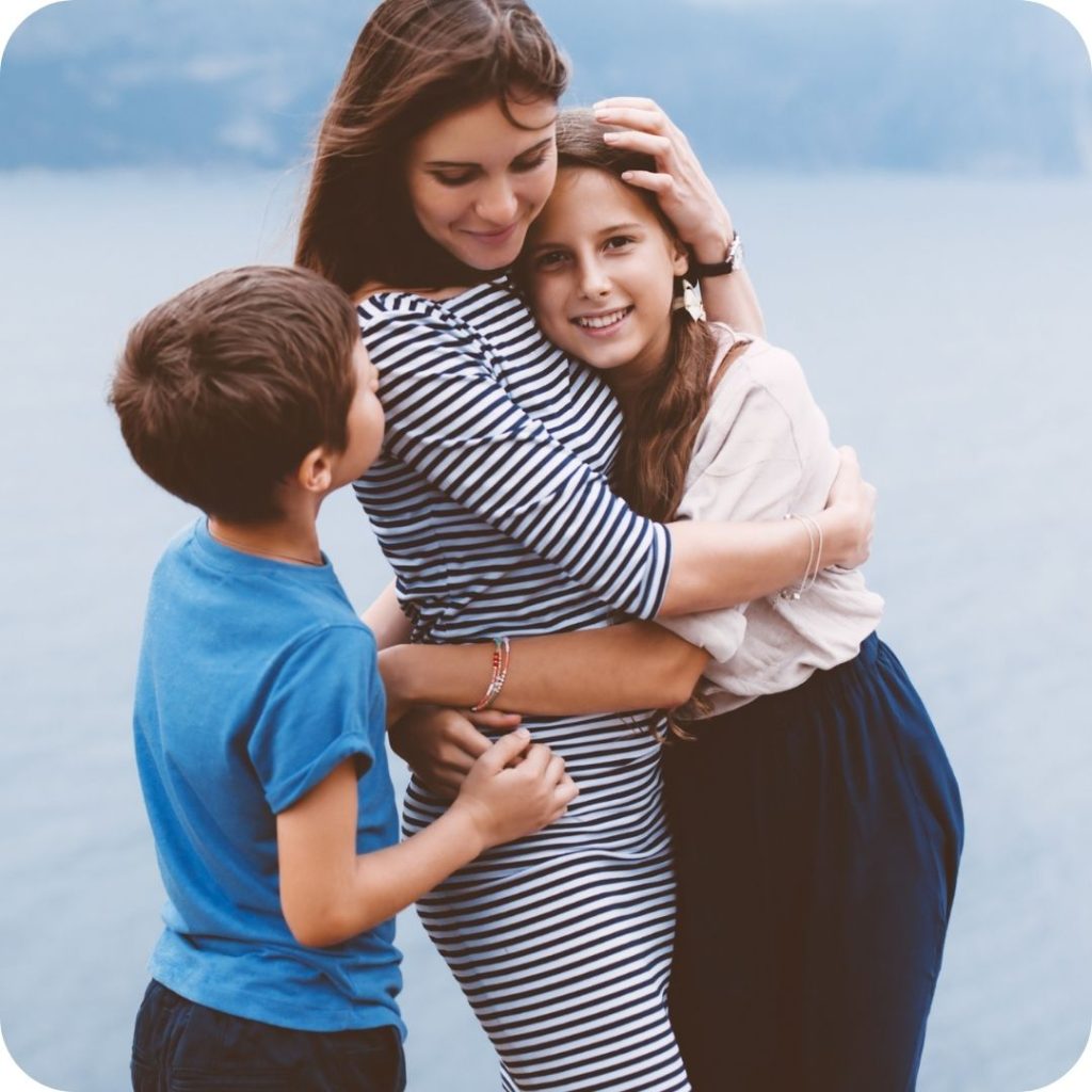 Woman embracing two children outdoors against blue sky