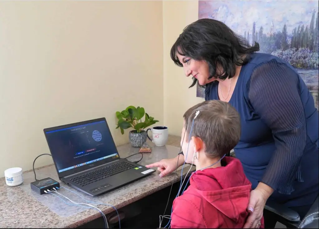 Dr. Roseann with child wearing neurofeedback cap at desk with laptop