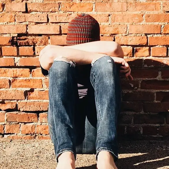 Person sitting against brick wall showing distress