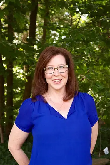 Professional headshot of therapist Nancy against outdoor foliage backdrop