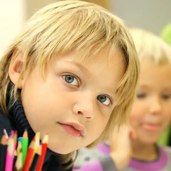 Child with thoughtful expression surrounded by colorful pencils