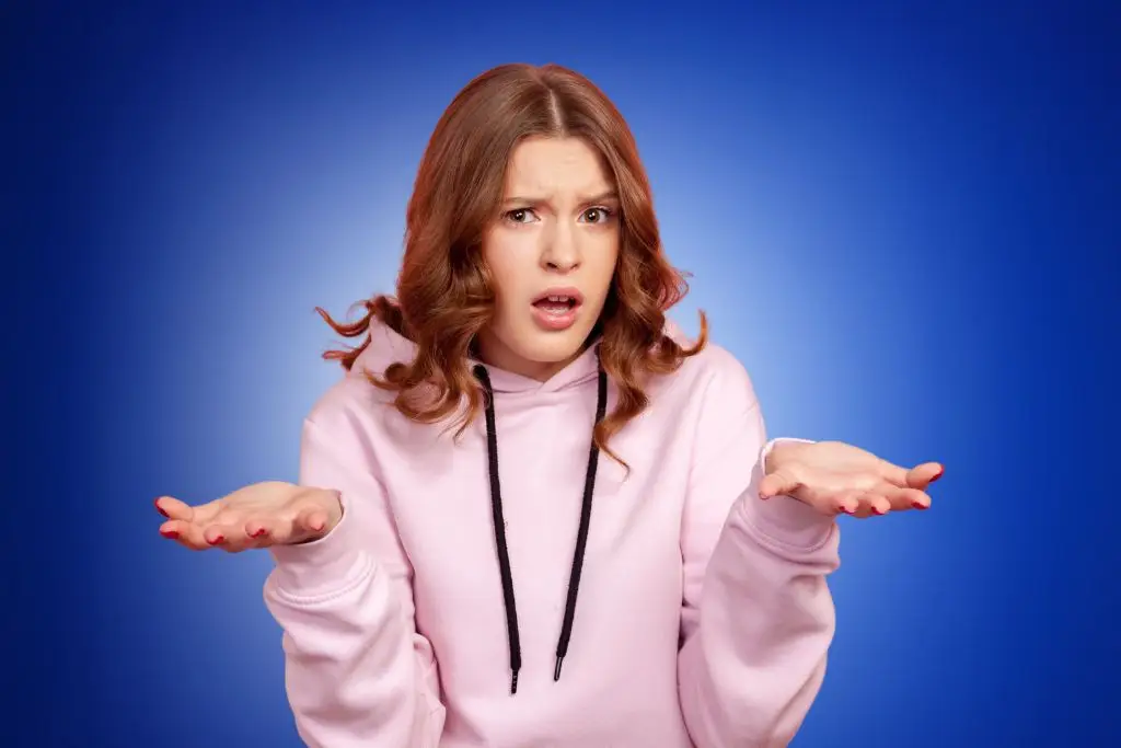Person in pink hoodie gesturing frustration against blue background