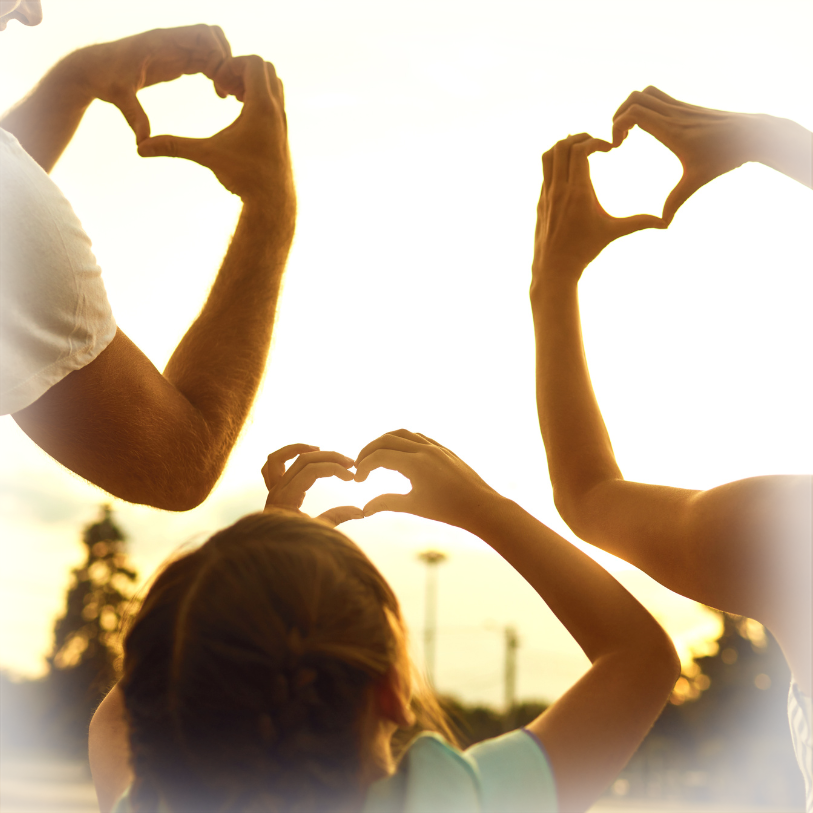 Multiple hands making heart shapes together backlit by sunset
