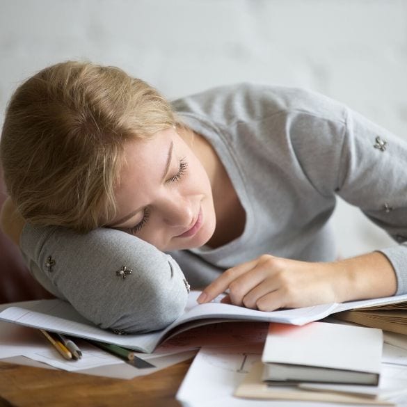 Young person resting their head on their arms over books