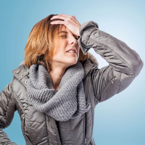 Person in winter clothing with hand to head against blue sky background