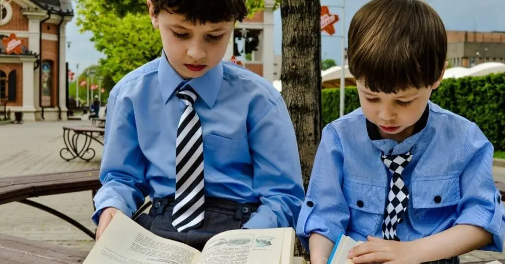 Two young boys reading book together outdoors
